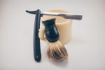 cheap razor leaning against mug. Beard brush next to cheap razor blades